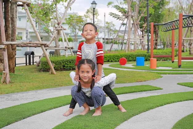 Menino asiático alegre e menina brincam de volta no jardim Irmão cavalgando nas costas da irmã