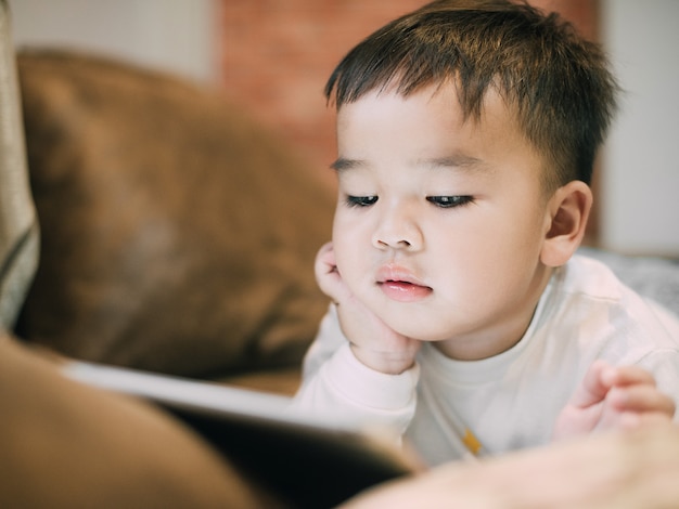 Foto menino asiático assistindo tablet muito perto usando como conceito de saúde e tecnologia