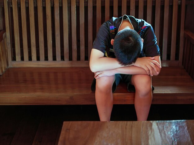 Menino asiático chateado sentado no escuro emoção triste e rosto triste crianças de depressão