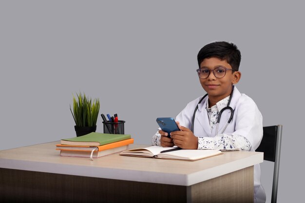 Foto menino asiático de 7 a 8 anos vestindo um avental de médico com um estetoscópio segurando um celular