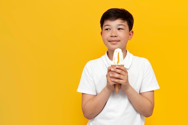 menino asiático de dez anos segurando uma casquinha de sorvete, sonhando e imaginando sobre fundo amarelo