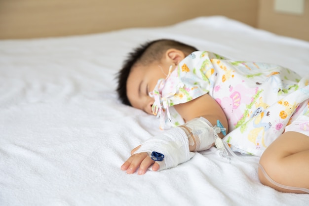 Menino asiático, dormindo na cama com infusão definida no departamento de crianças no hospital