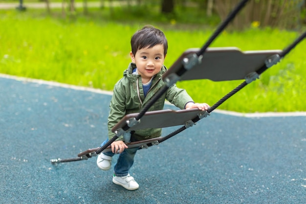 Menino asiático está brincando no playground de madeira com cara feliz no verão ao ar livre e olhando para a câmera com um sorriso