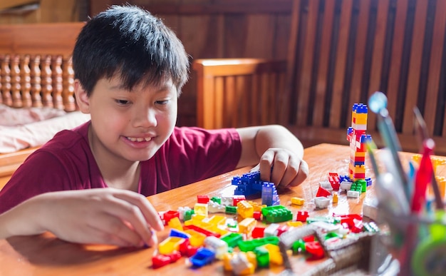 Menino asiático está ficando criativo com a montagem de brinquedos de tijolos de plástico coloridos em casa