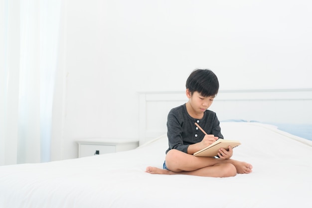 Menino asiático fazendo lição de casa em uma cama em casa