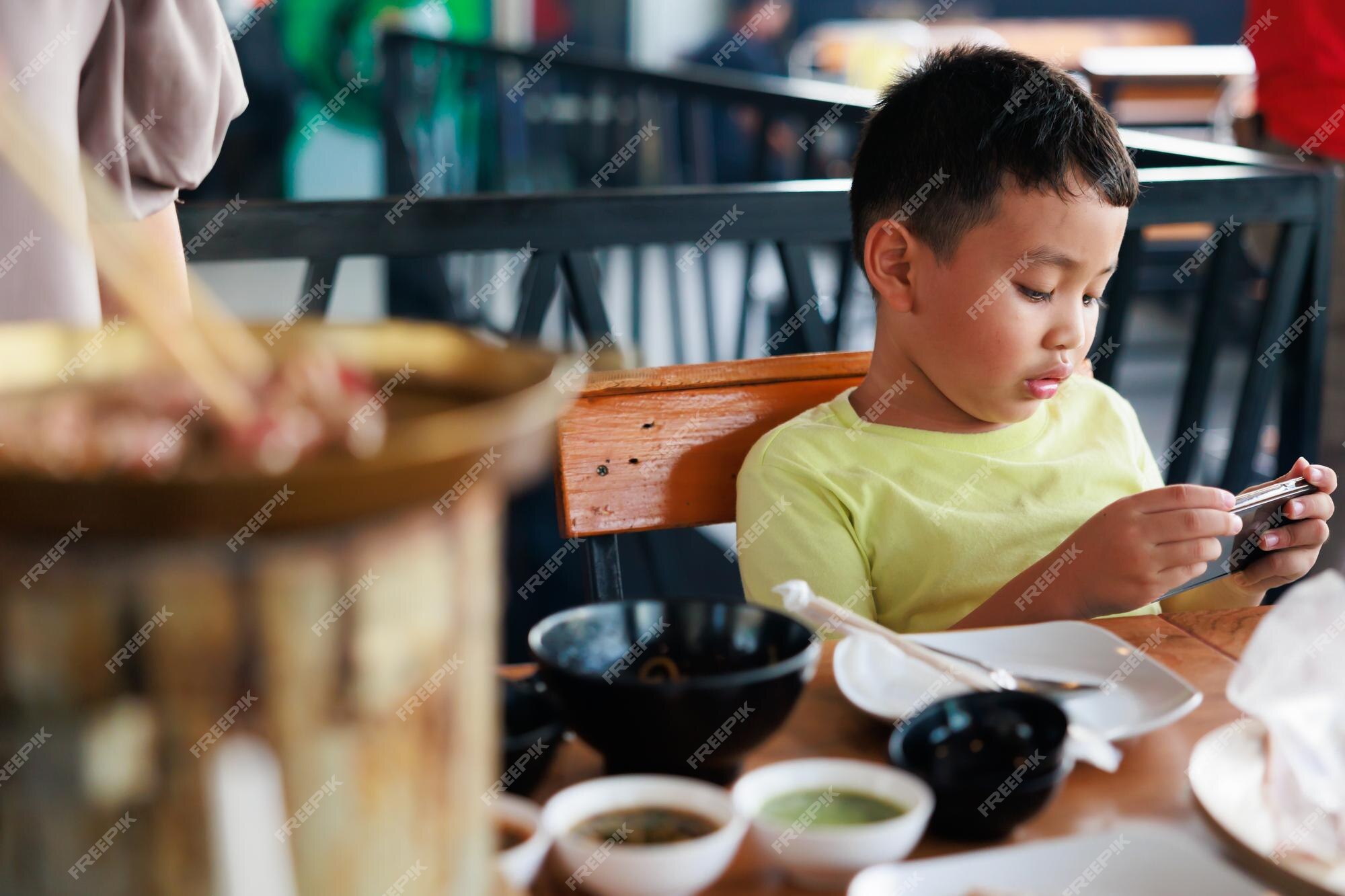 retrato menino jogando no celular enquanto espera por comida