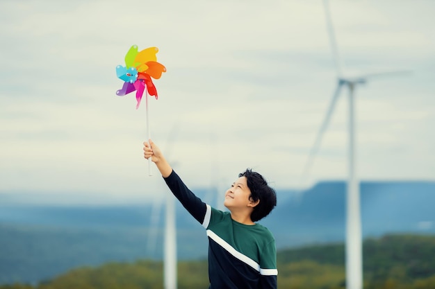 Menino asiático progressivo brincando com brinquedo de cata-vento na fazenda de turbinas eólicas