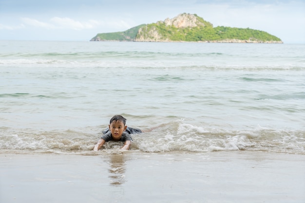 Menino asiático que aprecia no mar perto da praia em Ao Manao, Prachuap Khiri Khan, Tailândia