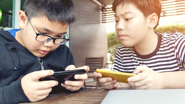 Menino asiático que joga o jogo móvel no telefone esperto junto.