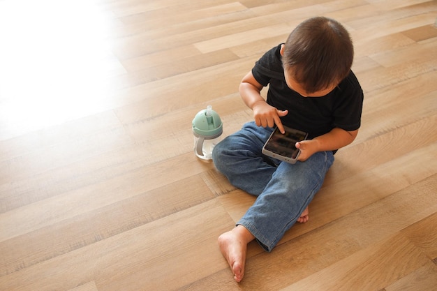 Menino asiático sentado no chão usando smartphone em casa jogando jogo para celular no celular