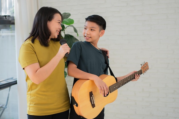 Menino asiático tocando violão e mãe cantando uma música e abraçando se sente apreciado e encorajado