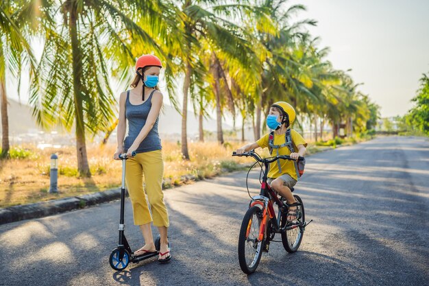 Menino ativo da escola e sua mãe com máscara médica e capacete de segurança andando de bicicleta com mochila