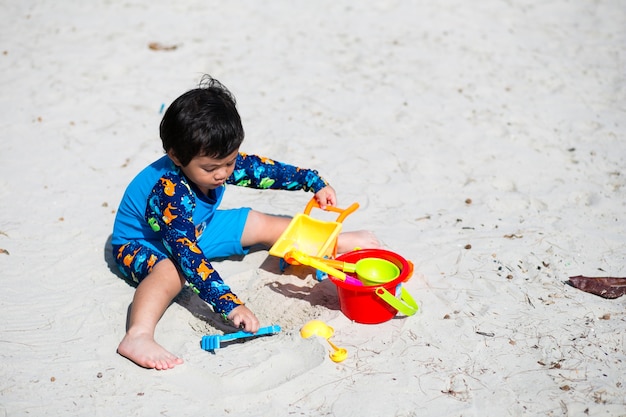 Menino bebê brincando com areia na costa do mar, tempo feliz na praia de verão