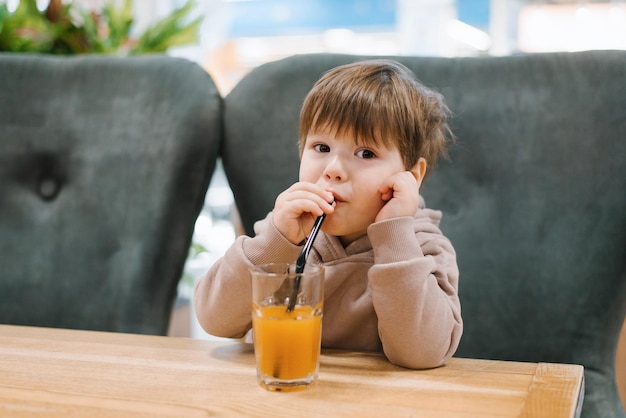 Menino bebe suco de canudo enquanto está sentado à mesa em um café