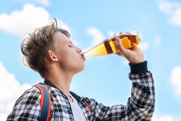 Menino bebendo limonada de uma garrafa em um belo fundo de céu azul