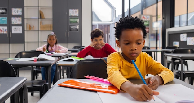 Menino biracial de amarelo se concentra em escrever em sua mesa em uma sala de aula da escola