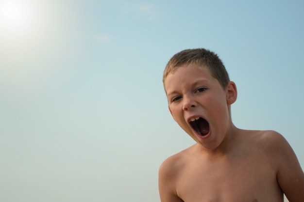 menino bocejando contra o céu azul em um dia ensolarado.