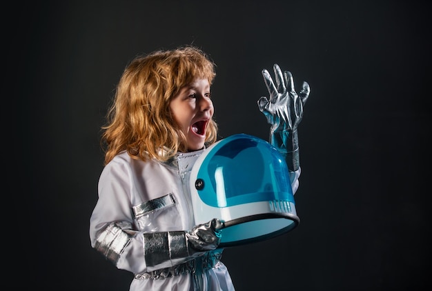 Foto menino bonitinho astronauta em traje espacial segurando capacete em fundo preto criança em um astronau