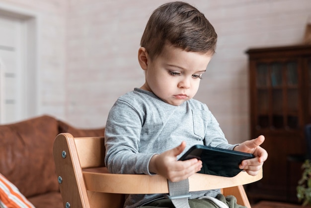 Menino bonitinho brincando com smartphone bebê saudável tocando o celular com os dedos parece...