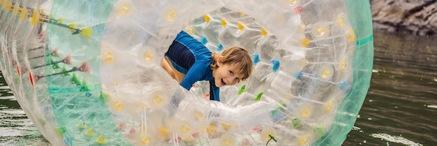 Menino bonitinho brincando em zorb, um anel cilíndrico de plástico rolante com um buraco no meio do