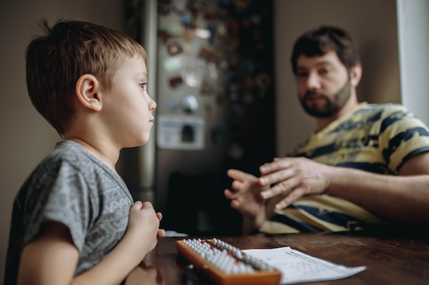 Menino bonitinho caucasiano fazendo sua lição de casa de aritmética mental com o pai sentado ao lado dele na mesa da cozinha. Foto de alta qualidade