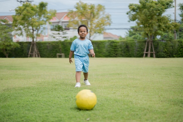 Menino bonitinho com bola de futebol no parque em um dia ensolarado