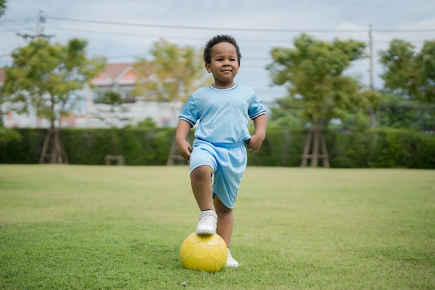 Menino bonitinho com bola de futebol no parque em um dia ensolarado