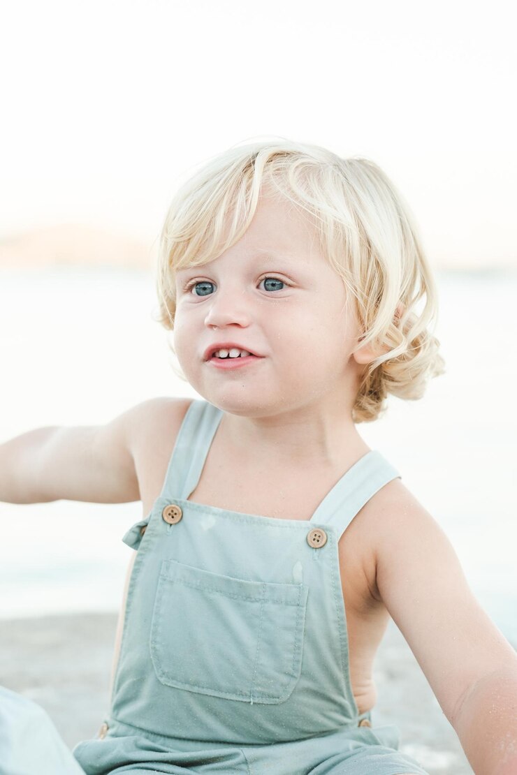Foto menino bonitinho com cabelo louro e olhos azuis em geral olhando para longe enquanto descansava na costa ensolarada