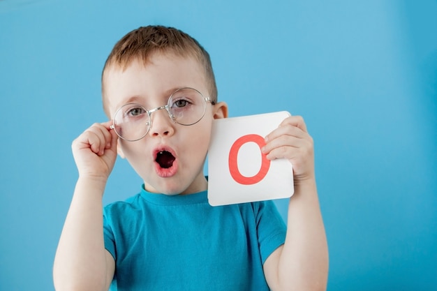 Menino bonitinho com carta na parede azul. criança aprendendo letras. alfabeto