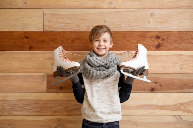 Menino bonitinho com patins de gelo contra madeira