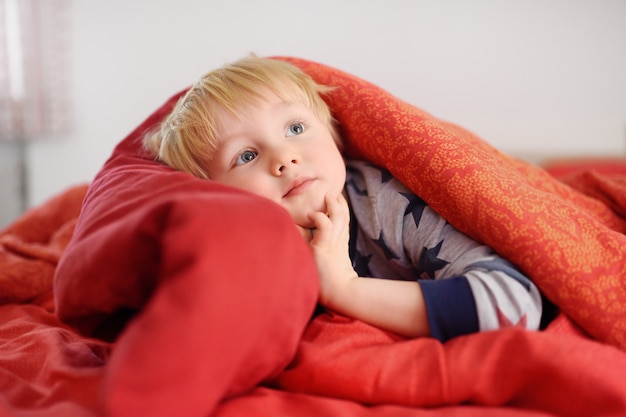 Menino bonitinho de pijama se divertindo na cama depois de dormir e assistir tv ou sonhando