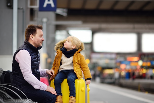 Menino bonitinho e seu pai esperando trem expresso na plataforma da estação ferroviária