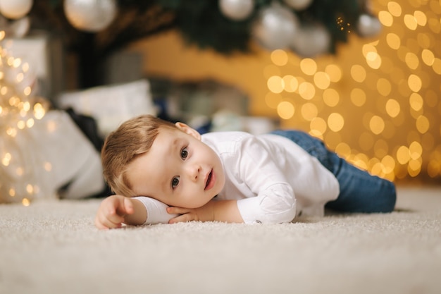 Menino bonitinho em casa perto da grande árvore de Natal à procura de presentes. Criança feliz passar o tempo de férias e aproveitar cada momento.