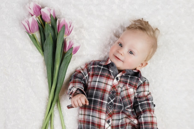 Foto menino bonitinho em uma camisa xadrez detém um buquê de tulipas cor de rosa