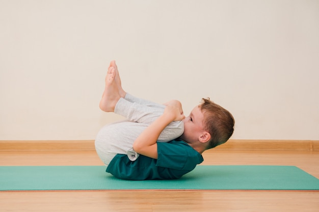 Menino bonitinho está aprendendo a fazer yoga no ginásio