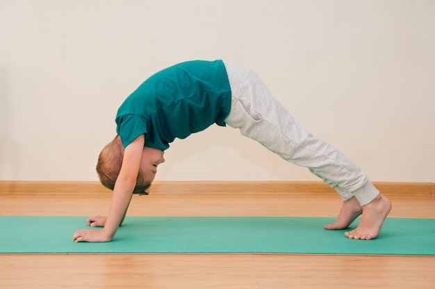 Menino bonitinho está aprendendo a fazer yoga no ginásio