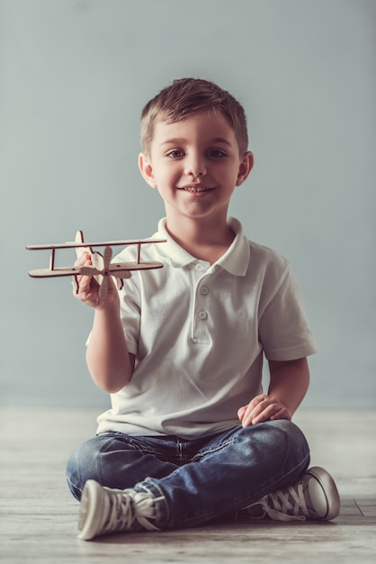 Menino bonitinho está brincando com o avião de brinquedo, olhando para a câmera