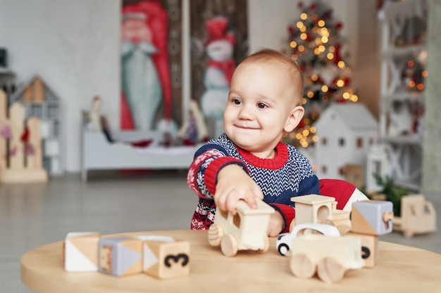 Menino bonitinho está brincando com o trem de brinquedo de madeira, carro de brinquedo, pirâmide e cubos, aprendendo o conceito de desenvolvimento. Desenvolvimento de habilidades motoras finas para crianças, imaginação e pensamento lógico