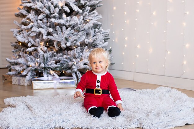 Menino bonitinho está sentado perto da árvore decorada para o Natal. Feliz Natal e Feliz Ano Novo.