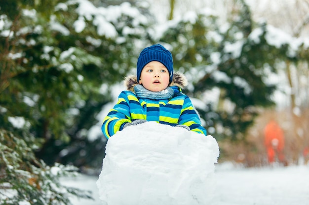 Menino bonitinho fazendo boneco de neve rolando grande bola de neve