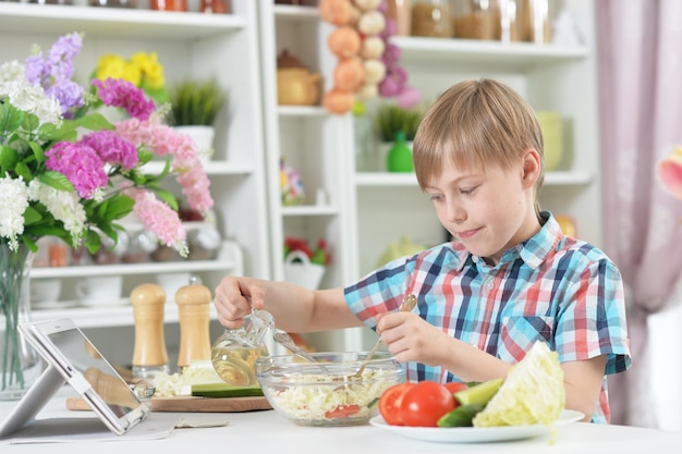 Menino bonitinho fazendo jantar na mesa da cozinha em casa