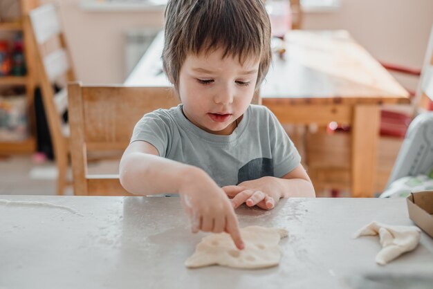 Menino bonitinho fazendo massa para biscoitos na cozinha