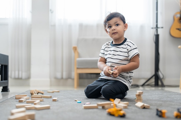 Menino bonitinho jogando jogo de pilhas de blocos de madeira no chão na sala de estar em casa