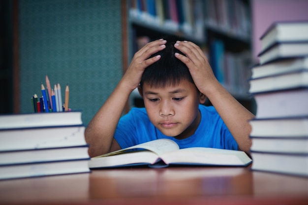 Menino bonitinho lendo livro na biblioteca