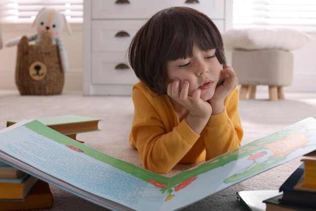 Menino bonitinho lendo livro no chão em casa