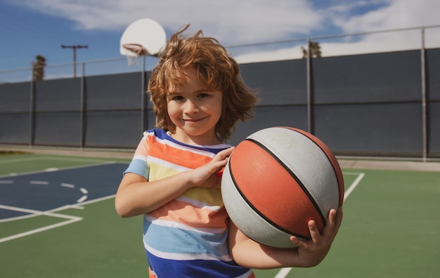 Menino bonitinho segurando uma bola de basquete tentando fazer um esporte de pontuação para crianças