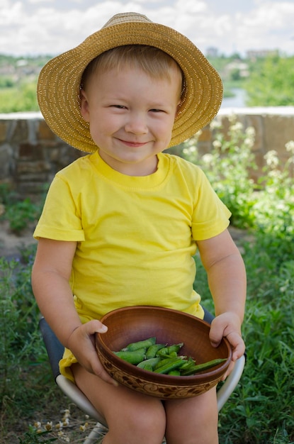 Menino bonitinho sorrindo e comendo legumes frescos fechados do lado de fora no verão Comida de verão colhida