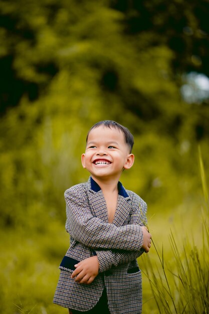 Menino bonitinho Um menino bem vestido de terno em um quintal com gramado e procurando algo interessante