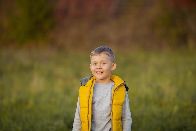 Menino bonito 5 anos de idade caminha no jardim outono. retrato de um menino feliz com roupas de outono brilhantes. outono quente e brilhante.