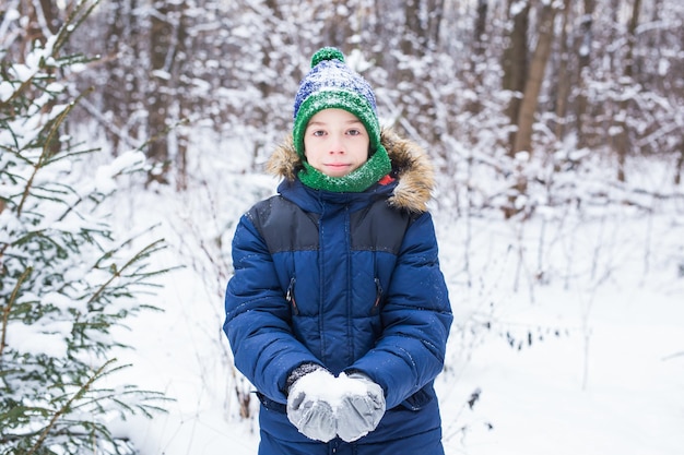 Menino bonito brinca com neve, divirta-se, sorri. Adolescente em winter park. Estilo de vida ativo, inverno